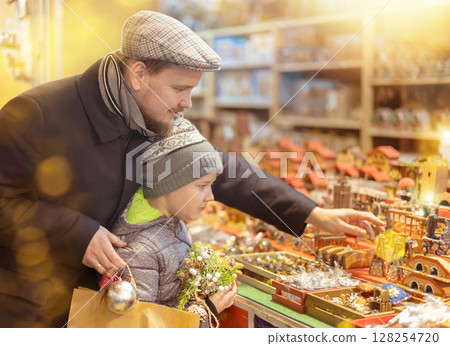 Dad and son standing near counter at Christmas market fair, choosing figurines for nativity scene 128254720