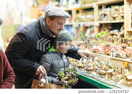 Dad and son standing near counter at Christmas market fair, choosing figurines for nativity scene 128254787
