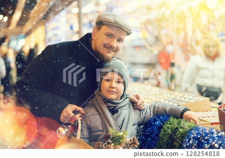 Man with son in outdoor souvenir shop examines Christmas toys Man with son in outdoor souvenir shop examines Christmas toys 128254818