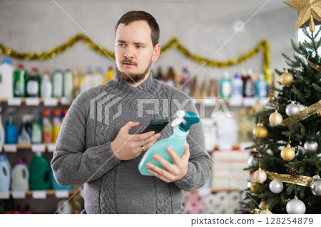 Man scanning cleaning spray bottle with phone in festively decorated store 128254879