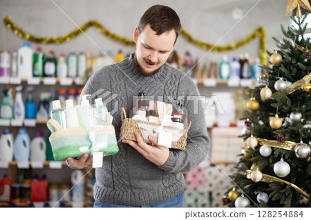 Young man choosing Christmas gift set with self-care products in store Young man choosing Christmas gift set with self-care products in store 128254884