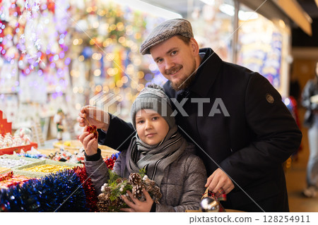 Man with son in outdoor souvenir shop examines Christmas toys Man with son in outdoor souvenir shop examines Christmas toys 128254911