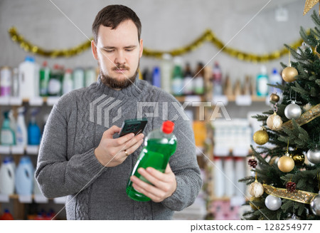 Young shopper scanning bottle of dishwashing liquid in festively decorated store Young shopper scanning bottle of dishwashing liquid in festively decorated store 128254977