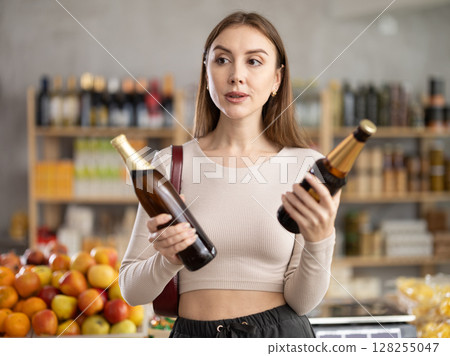 Girl hold packages bottle tin and choose consider beer in store 128255047