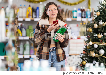 In Christmas decorated shop, woman client scanning QR code on package dishwashing liquid gel In Christmas decorated shop, woman client scanning QR code on package dishwashing liquid gel 128255052