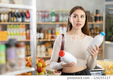 Girl hold packages bottles and choose consider milk in store Girl hold packages bottles and choose consider milk in store 128255117