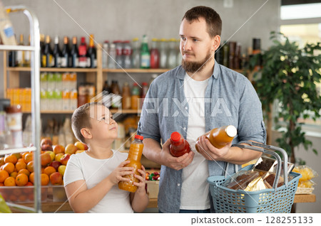Preteen boy with father choosing juice in bottles in grocery store Preteen boy with father choosing juice in bottles in grocery store 128255133