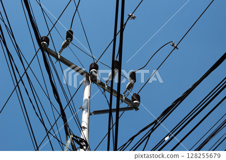 Tangled network of overhead power lines and cables against a clear blue sky. 128255679