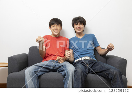 teen boys watching television at home in living room, watching football match at home. 128259132