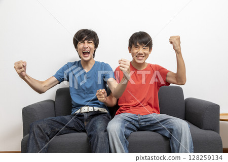 teen boys watching television at home in living room, watching football match at home. 128259134