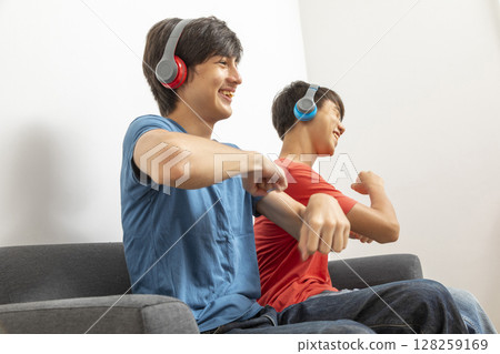 Two teenager boys listening to music with headphones in living room. Two teenager boys listening to music with headphones in living room. 128259169