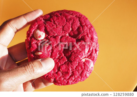 Bright red cookie held against a vibrant orange background 128259880