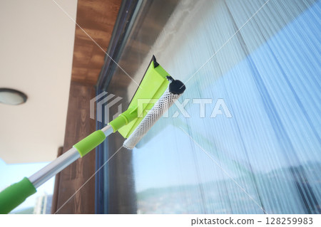 Cleaning glass surfaces with a green squeegee tool 128259983
