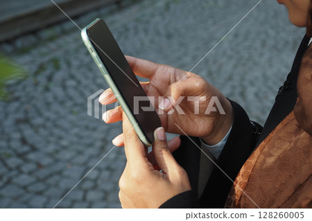 Person using smartphone outdoors in a city setting 128260005