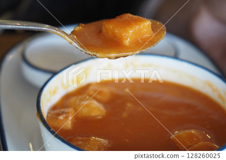 Warm pumpkin soup with diced vegetables served in bowl 128260025