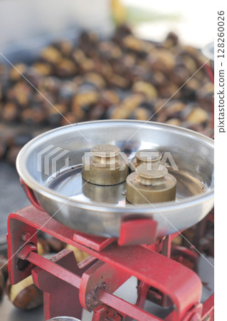 Weighing roasted chestnuts on a traditional scale 128260026