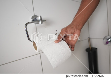 Hand reaching for toilet paper in a bathroom setting Hand reaching for toilet paper in a bathroom setting 128260209