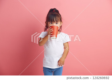 Handsome little asian girl drinking from disposable paper cup standing over pink isolated background. Handsome little asian girl drinking from disposable paper cup standing over pink isolated background. 128260692