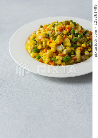 This dish features a vibrant salad composed of boiled eggs, tender chicken breast, diced potatoes, sweet carrots, and fresh green peas, all topped with a drizzle of olive oil for flavor 128261499