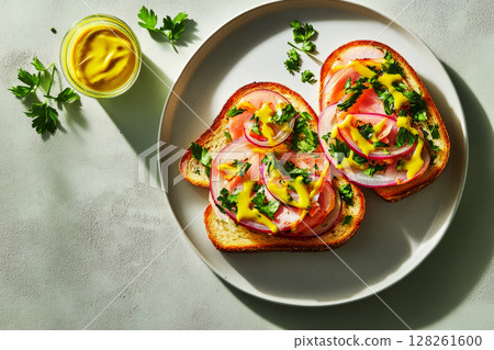 A delicious breakfast featuring toasted bread layered with slices of tomato, onion, and herbs, drizzled with mustard on a simple plate. Perfect for a healthy start to the day 128261600