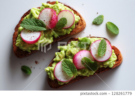 Brightly colored breakfast includes slices of toasted bread layered with creamy avocado, garnished with fresh radishes and mint leaves, perfect for a sunny morning 128261779