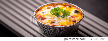 Four individual breakfast cups filled with egg, broccoli, and bell peppers are beautifully arranged on a sleek black tray, offering a hearty morning meal option, banner 128261783
