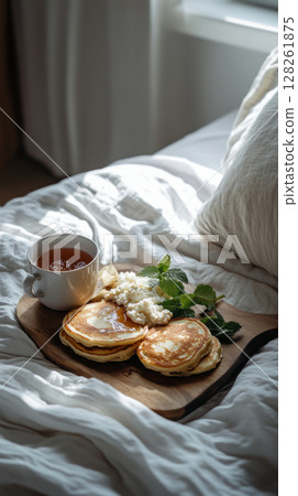 A beautifully arranged breakfast board featuring golden pancakes, rich coffee, and fresh fruit rests on a tray atop soft bedding. Natural light streams in through a nearby window A beautifully arranged breakfast board featuring golden pancakes, rich coffee, and fresh fruit rests on a tray atop soft bedding. Natural light streams in through a nearby window 128261875