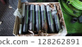 A crate of newly manufactured flange studs, steel threaded rods, with industrial machinery in the background. Close-up of metal flange studs, packaged in a wooden box for transport. Metal studs  128262891