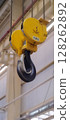 Heavy-duty crane hook with a 10-ton capacity. Yellow hoist and black steel hook. Industrial equipment for lifting heavy loads. Large industrial crane hook with safety catch, suspended in the workshop. 128262892