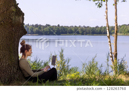 A woman works outdoors by a serene lakeside, enjoying natures beauty and tranquility A woman works outdoors by a serene lakeside, enjoying natures beauty and tranquility 128263768