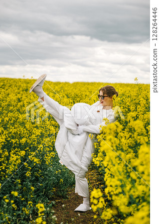 Woman joyfully posing in a field of bright yellow flowers on a cloudy day 128264446