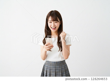 A Japanese woman posing in a fist pump while looking at her smartphone screen (white background, for cutting) 128264653
