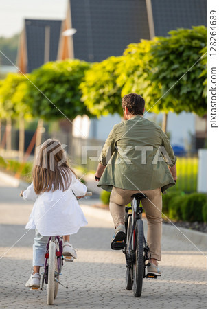 Back view of parent and child enjoying family bike walk on residential trail Back view of parent and child enjoying family bike walk on residential trail 128264689