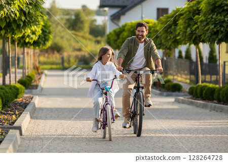 Family bike ride with father and daughter on park path near home Family bike ride with father and daughter on park path near home 128264728