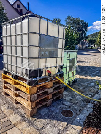 Large plastic water storage tanks on wooden pallets with yellow hose outdoors. High quality photo 128264894