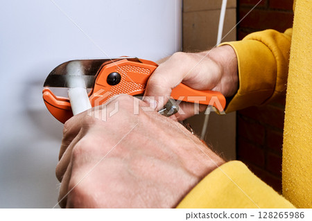 Ratchet pipe cutter slices multilayer pipe as hands operate tool during pipe cutting process for plumbing work. 128265986