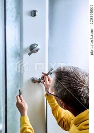 Plumber uses wrench to tighten metal nut on shower hose connection, securing fitting to wall of shower cabin and preventing water leakage during use. 128266005