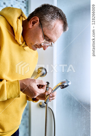 Inside shower cabin plumber inspects rubber gasket of shower hose connector before replacing leaking flexible hose with new fitting. Inside shower cabin plumber inspects rubber gasket of shower hose connector before replacing leaking flexible hose with new fitting. 128266009