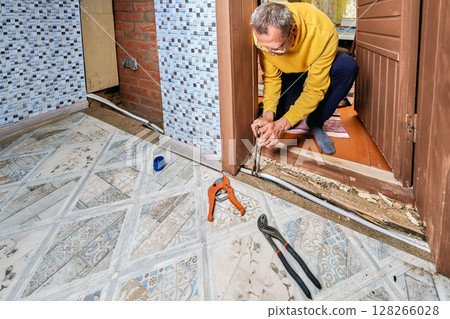 Plumber uses two open end wrenches to tighten securing nuts of compression coupling on multilayer pipe during installation of plumbing connection near doorway. 128266028