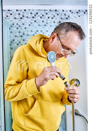 Connecting showerhead to flexible hose plumber twists threaded end of handheld unit onto fitting above shower floor, vertical image. 128266032