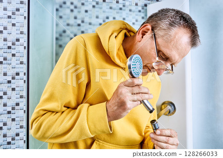 Attaching handheld showerhead to flexible hose, plumber connects threaded fitting by rotating head onto metal end inside shower cabin. 128266033