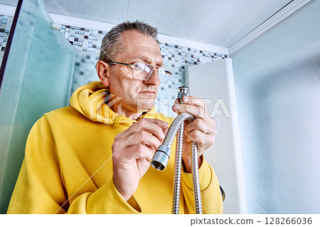 Plumber inside shower cabin examines rubber gasket of shower hose connector before replacing leaking flexible hose with new fitting. Plumber inside shower cabin examines rubber gasket of shower hose connector before replacing leaking flexible hose with new fitting. 128266036