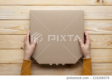 Pizza closed carton box in human caucasian hands on natural wooden table flat lay mockup with blank space 128266079