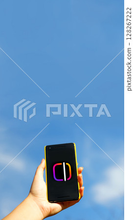 A hand holding a smartphone displaying a blue social media app interface, actively engaged in video creation and edits for Instagram Reels or a story on the platform A hand holding a smartphone displaying a blue social media app interface, actively engaged in video creation and edits for Instagram Reels or a story on the platform 128267222