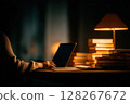 Man working late at desk with laptop and warm lamp light 128267672