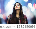 Young woman looking up at city lights with a gently smile 128269064