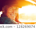 Senior farmer smiling and driving tractor during golden hour 128269074