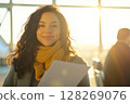 Young woman smiling and holding documents in airport terminal at sunset 128269076