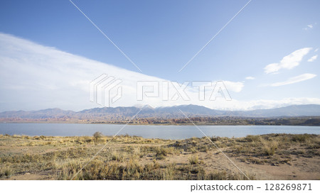 the lake of Issyk kul and the wide meadow in kyrgyzstan with the tian shan mountain range background the lake of Issyk kul and the wide meadow in kyrgyzstan with the tian shan mountain range background 128269871