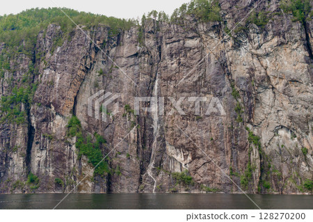 Tall narrow waterfall on steep fjord cliff near Bergen, Norway 128270200